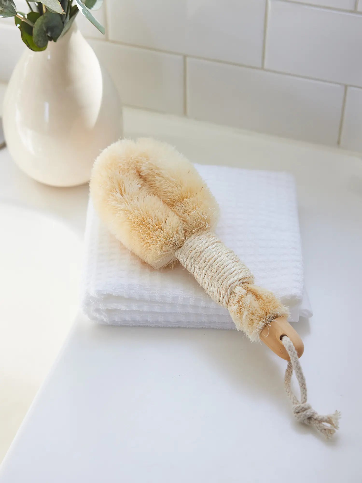 Skin-Smoothing Body Brush from Juniper Loft Soap Company lays on a white towel on a bathroom counter