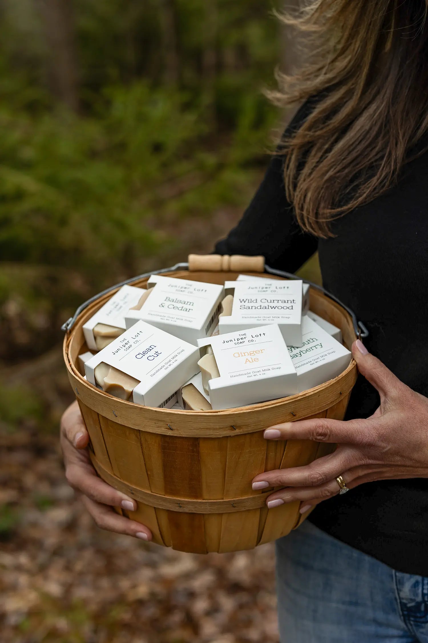 Closeup of a Juniper Loft founder Christina holding a basket with several bars of packaged goat milk soap