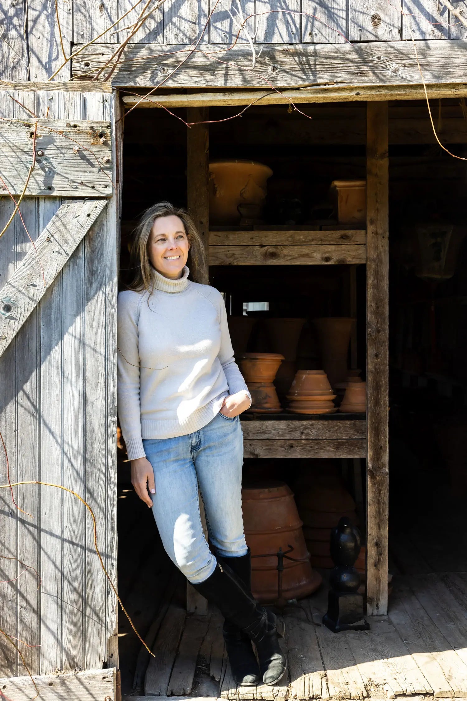 Juniper Loft founder Christina stands in the doorway of an old barn with terracotta pots behind her