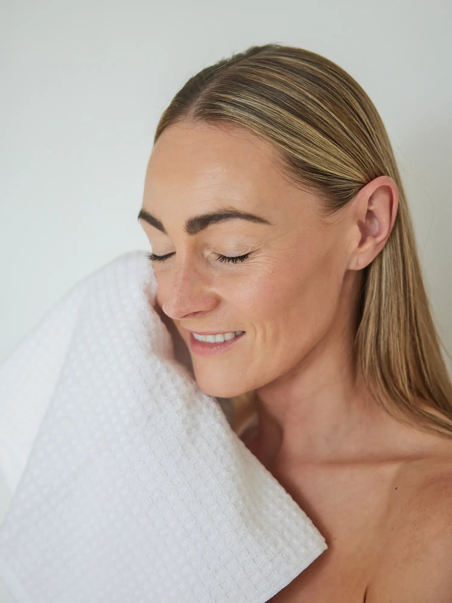 Woman with a white towel wrapped around her shoulders against a plain background