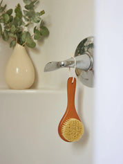 Juniper Loft Soap Company dry body brush hanging from a bathtub lever