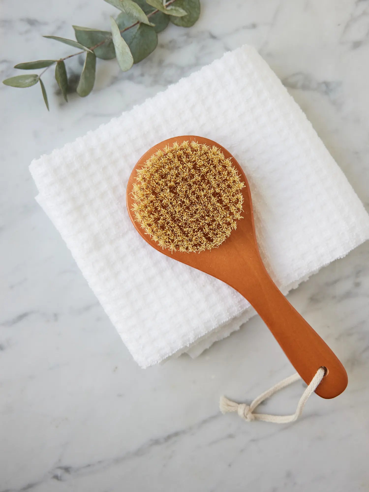 Juniper Loft Soap Company dry body brush on a white towel on top of a gray marble countertop