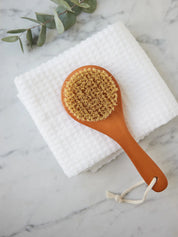 Juniper Loft Soap Company dry body brush on a white towel on top of a gray marble countertop