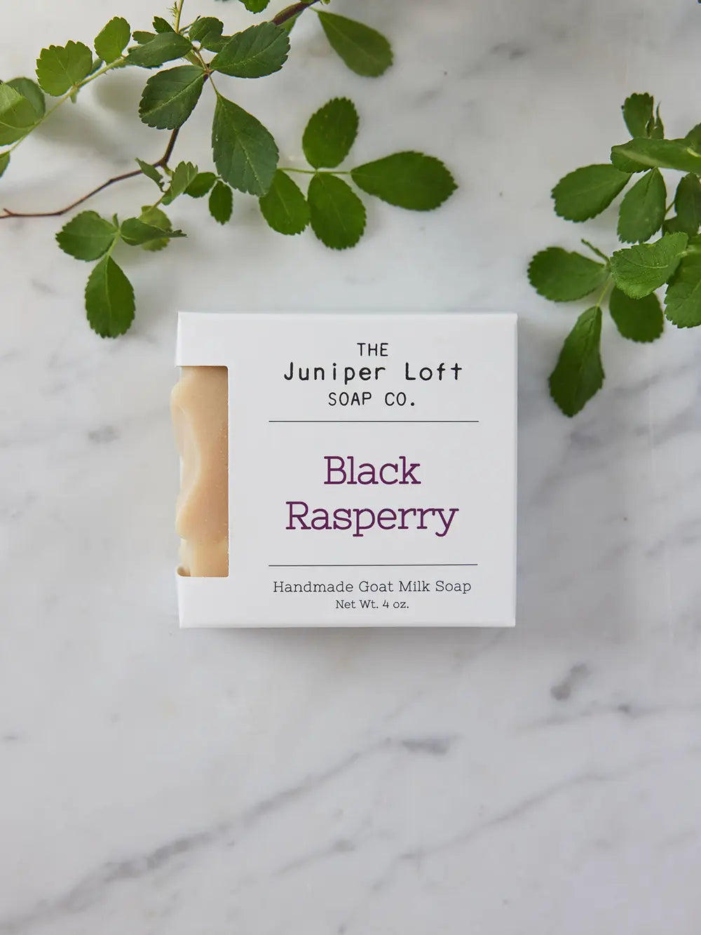 Bar of Black Raspberry soap from Juniper Loft Soap Company with some raspberry leaves around it