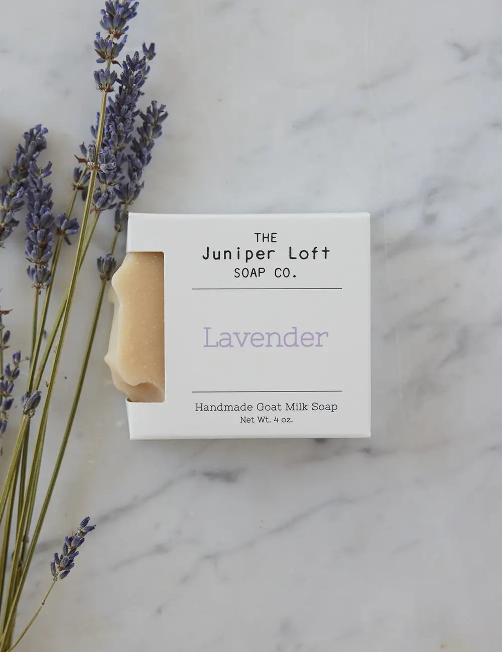 A few sprigs of lavender sit next to a bar of Lavender soap from Juniper Loft Soap Company