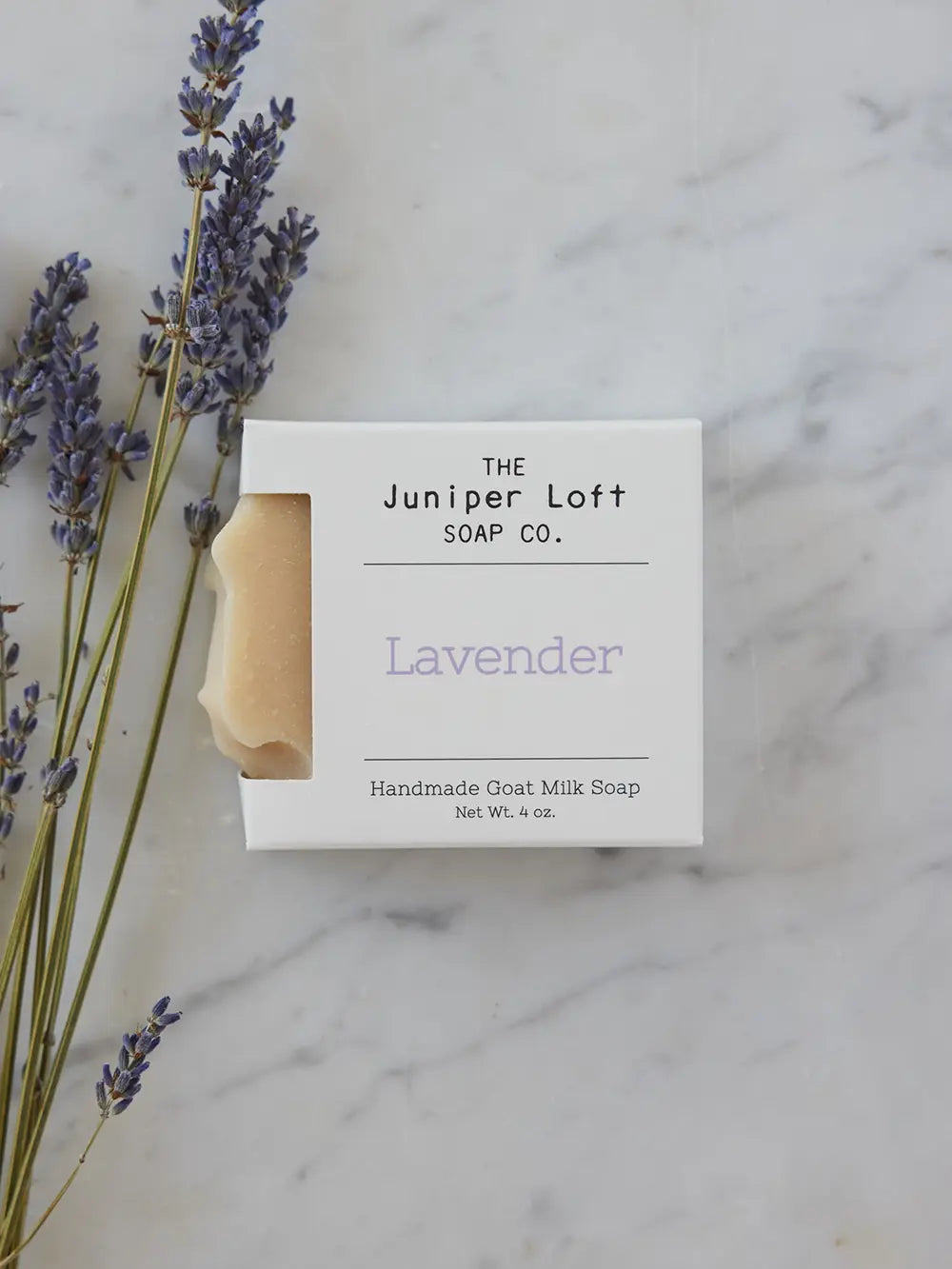 A few sprigs of lavender sit next to a bar of Lavender soap from Juniper Loft Soap Company