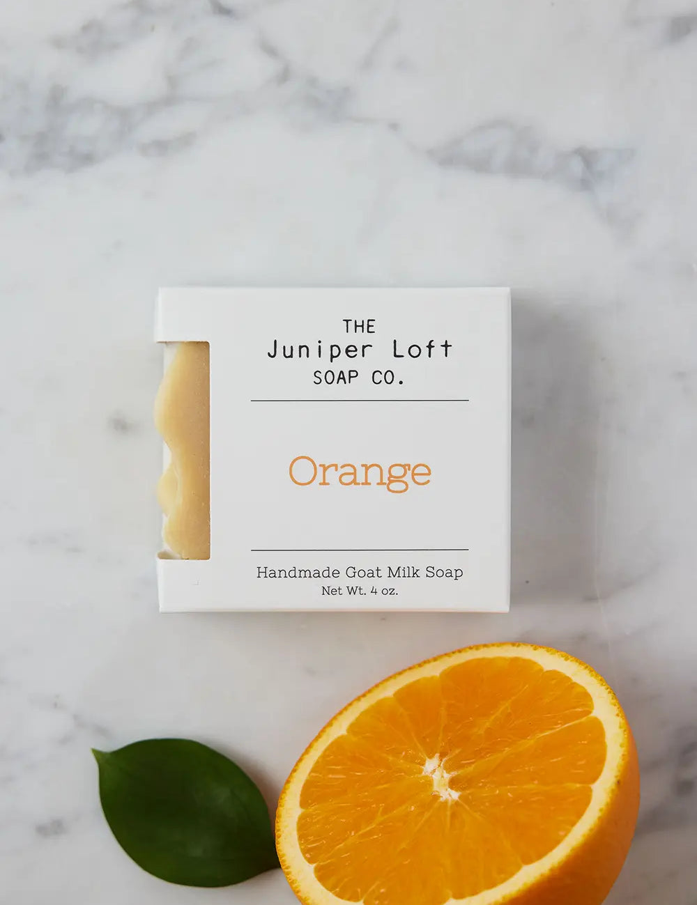 Bar of Orange soap from Juniper Loft Soap Company next to half a sliced orange