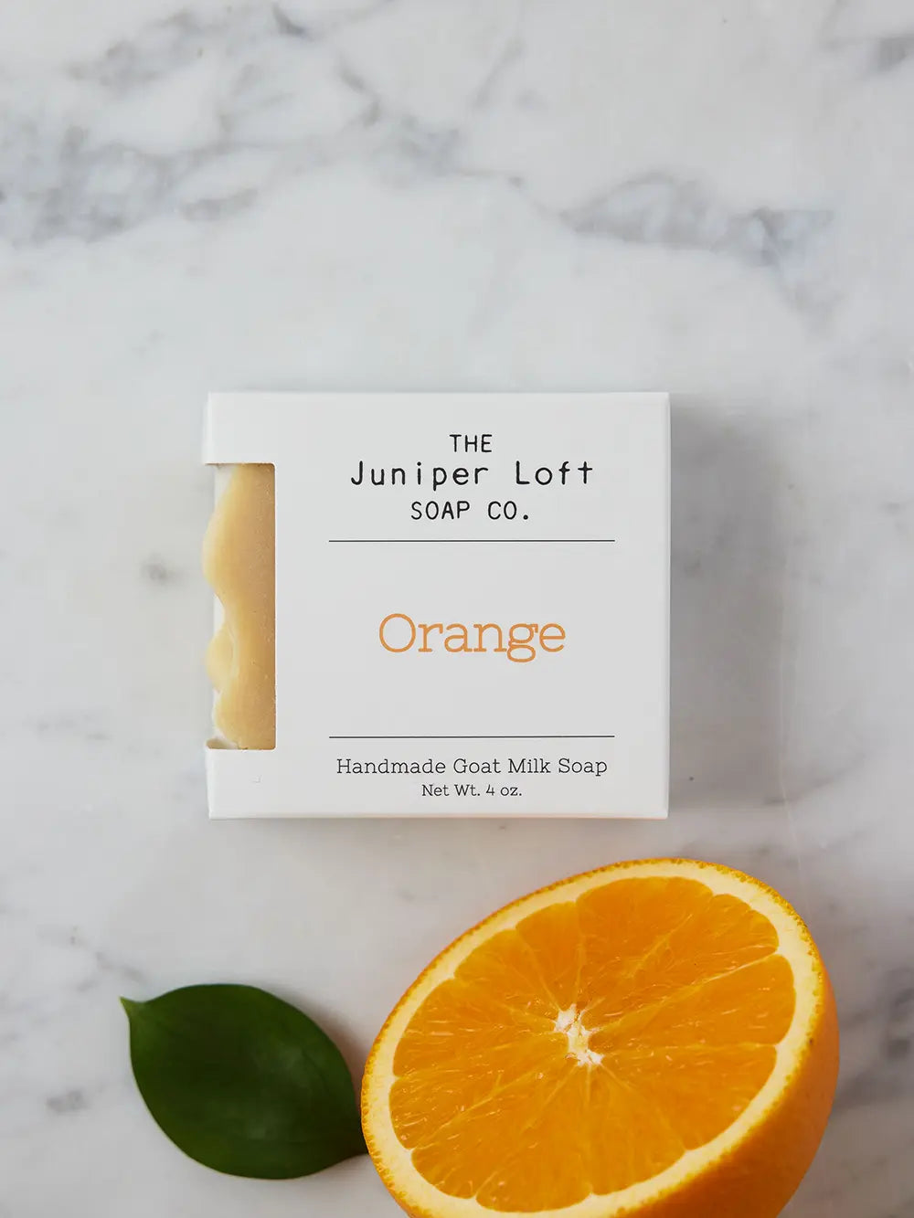 Bar of Orange soap from Juniper Loft Soap Company next to half a sliced orange