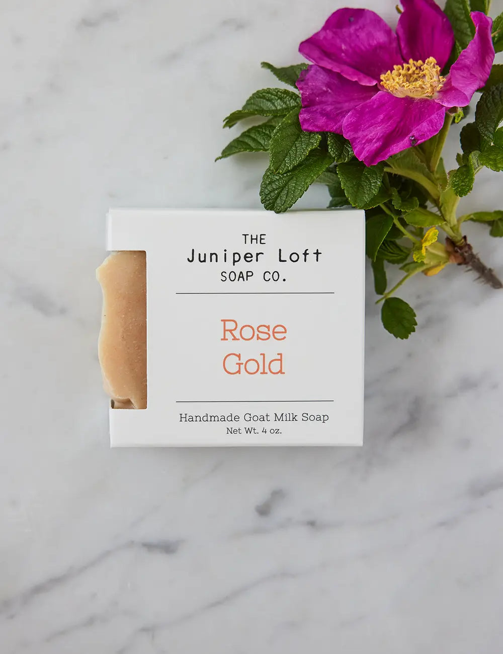 Bar of Rose Gold soap from Juniper Loft Soap Company with a bright pink flower beside it