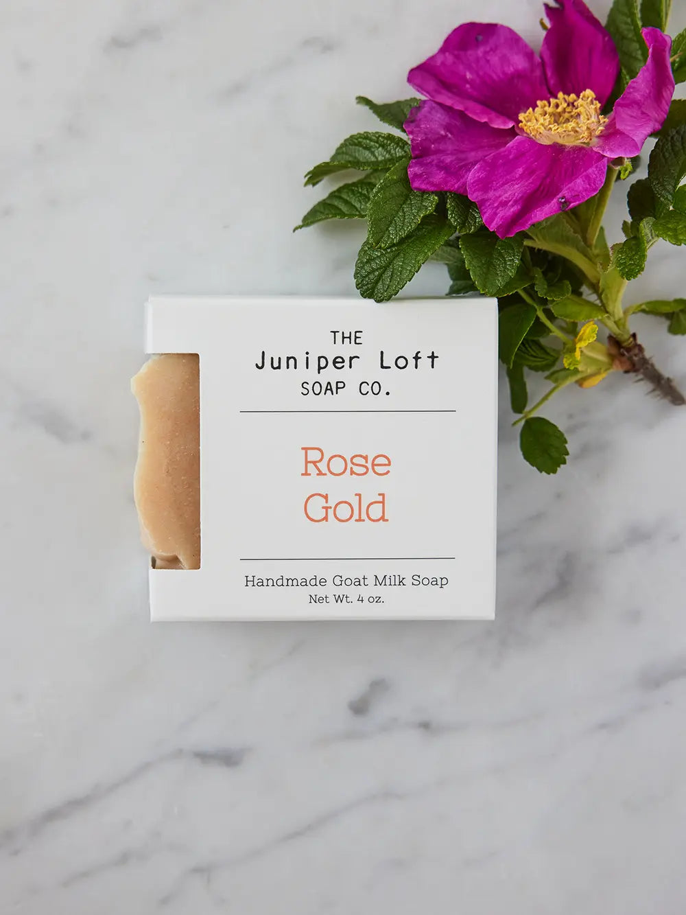 Bar of Rose Gold soap from Juniper Loft Soap Company with a bright pink flower beside it