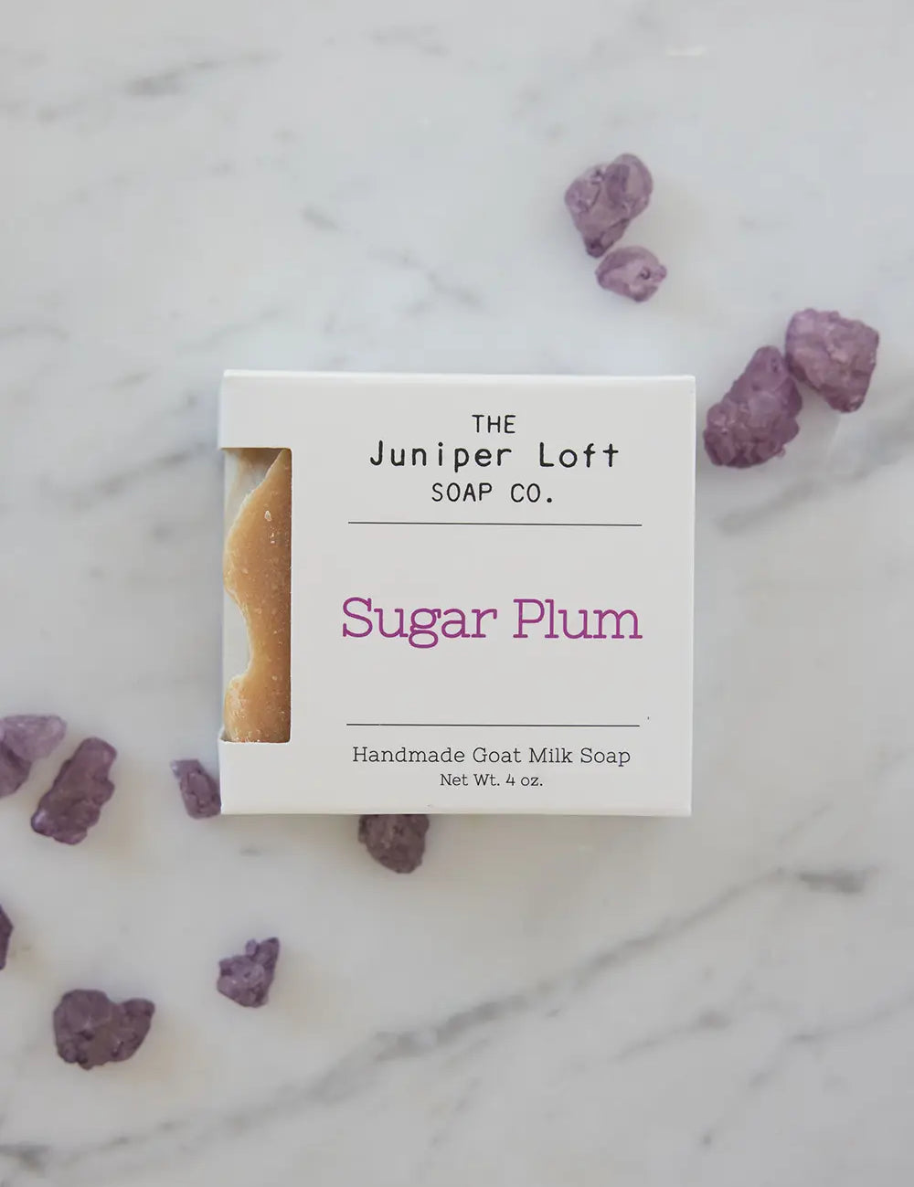 Bar of Sugar Plum soap from Juniper Loft Soap Company beside a handful of purple amethyst gems