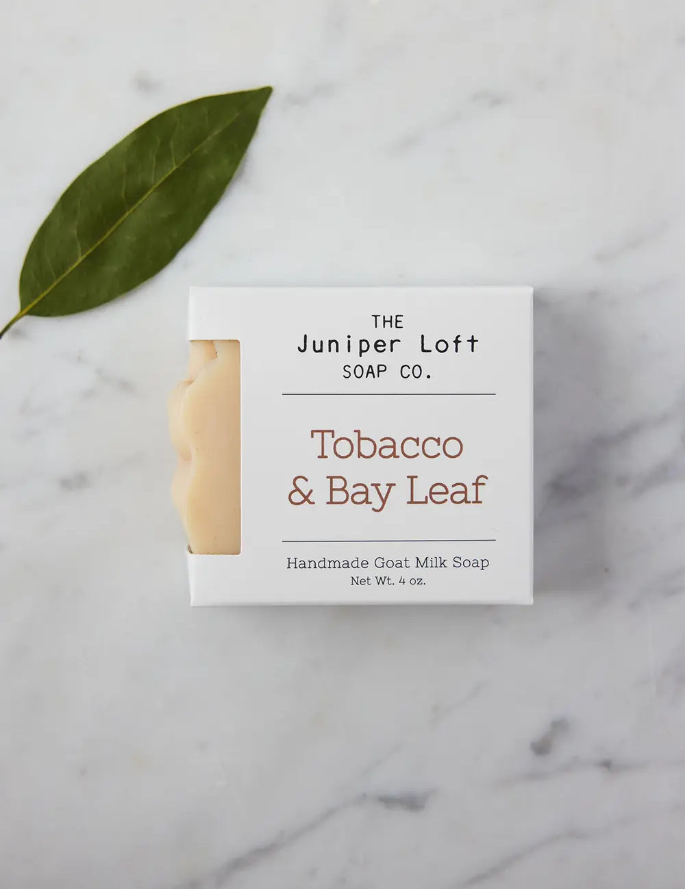 Bar of Tobacco and Bay Leaf soap from Juniper Loft Soap Company laying next to a single bay leaf