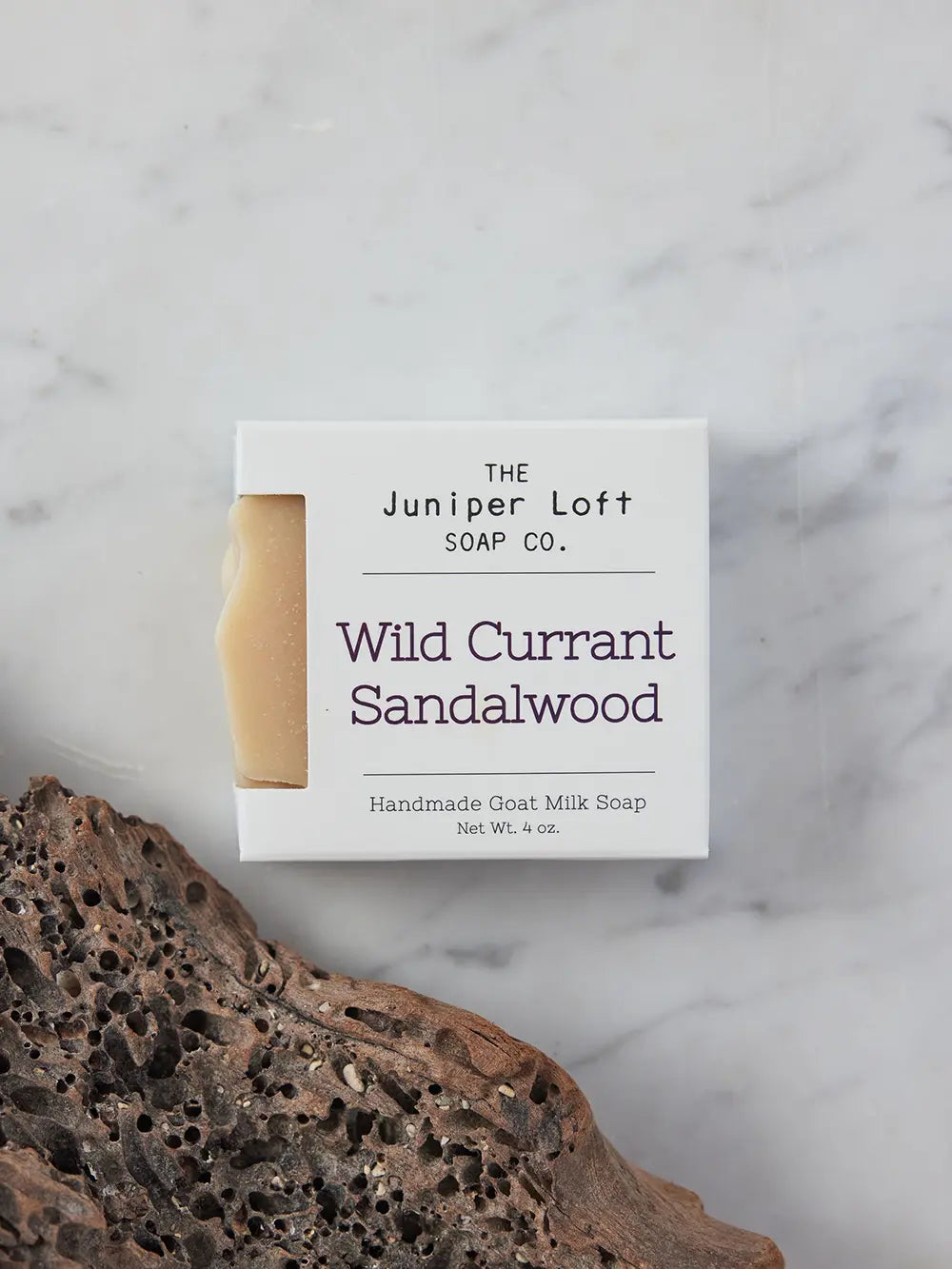 Bar of Wild Currant and Sandalwood soap from Juniper Loft Soap Company next to a porous piece of sandalwood