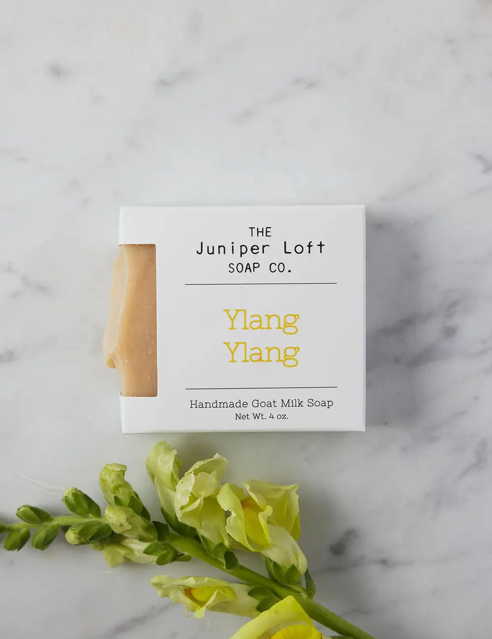 Bar of Ylang Ylang soap from Juniper Loft Soap Company next to a stem of yellow snapdragon