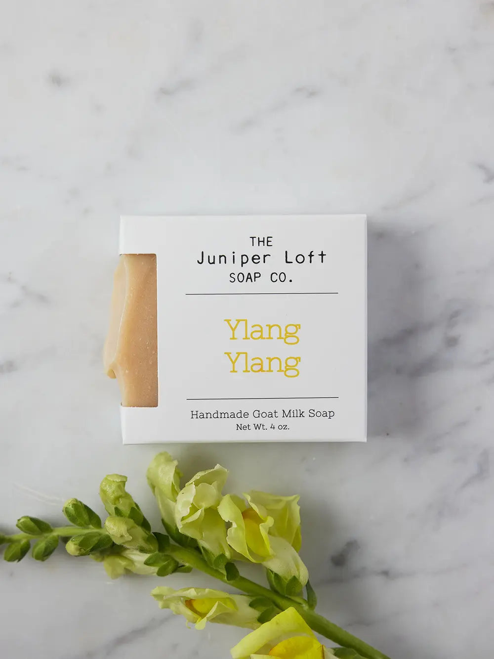 Bar of Ylang Ylang soap from Juniper Loft Soap Company next to a stem of yellow snapdragon