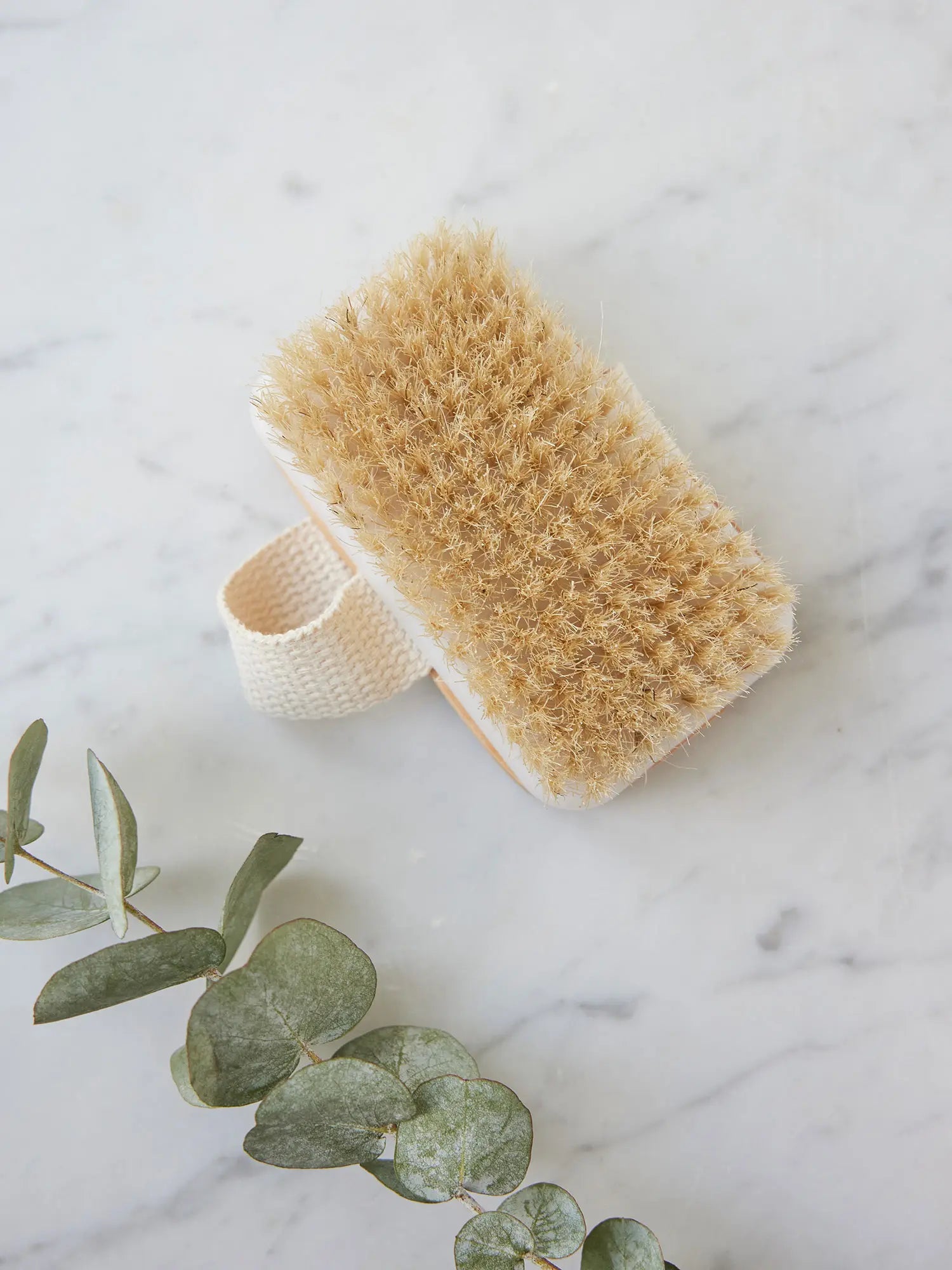 Detached brush head from a long-handled bath brush from Juniper Loft Soap Company on a gray marble countertop