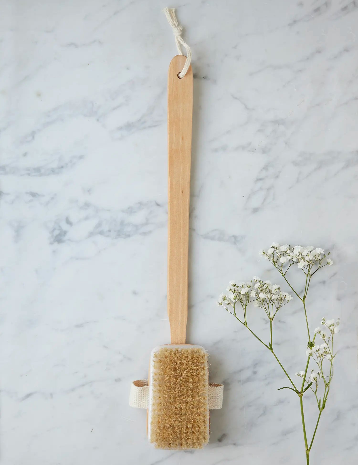 Long-handled bath brush from Juniper Loft Soap Company on a gray marble countertop with a sprig of baby's breath