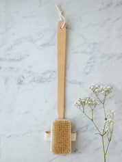 Long-handled bath brush from Juniper Loft Soap Company on a gray marble countertop with a sprig of baby's breath