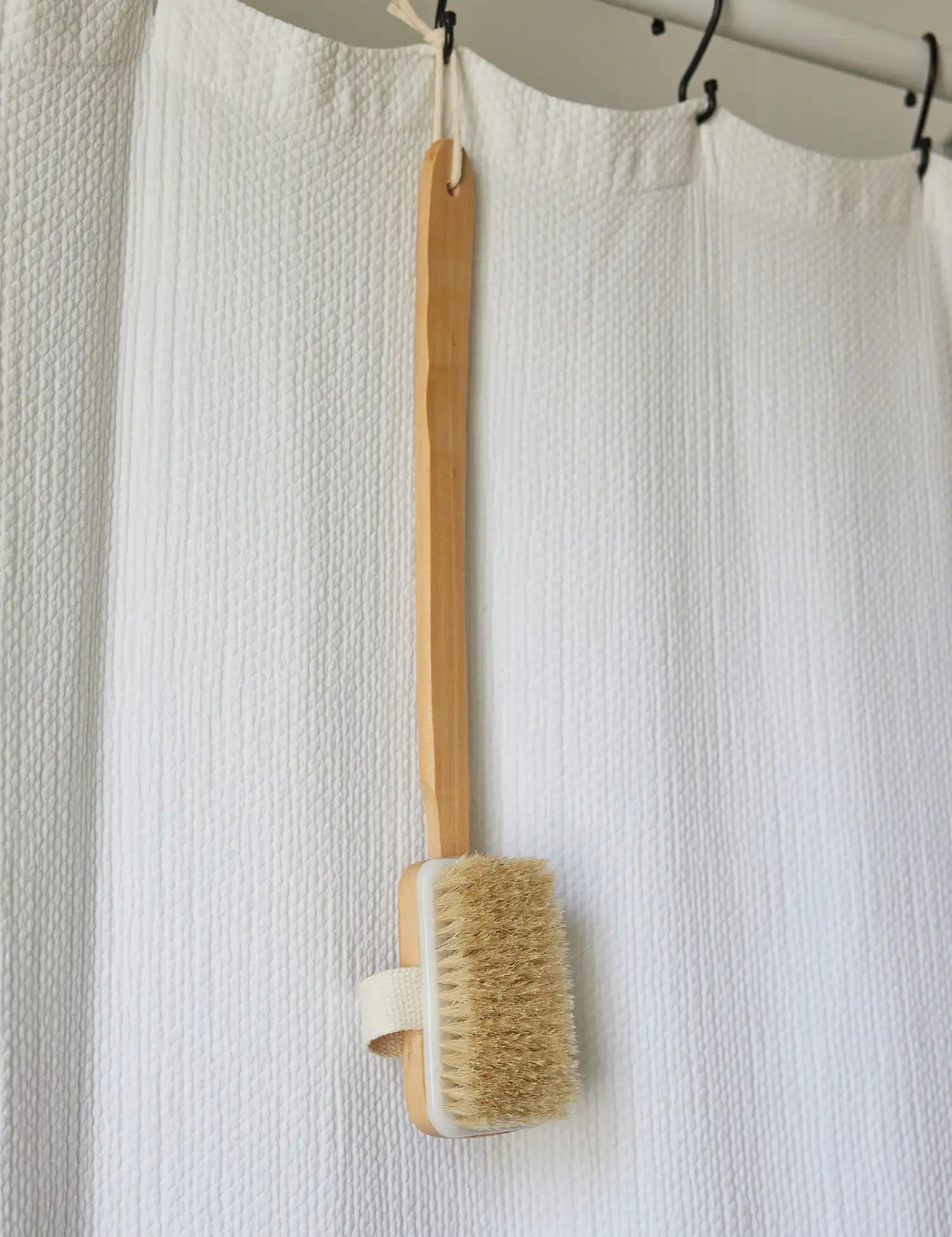 Long-handled bath brush from Juniper Loft Soap Company hanging from a white shower curtain
