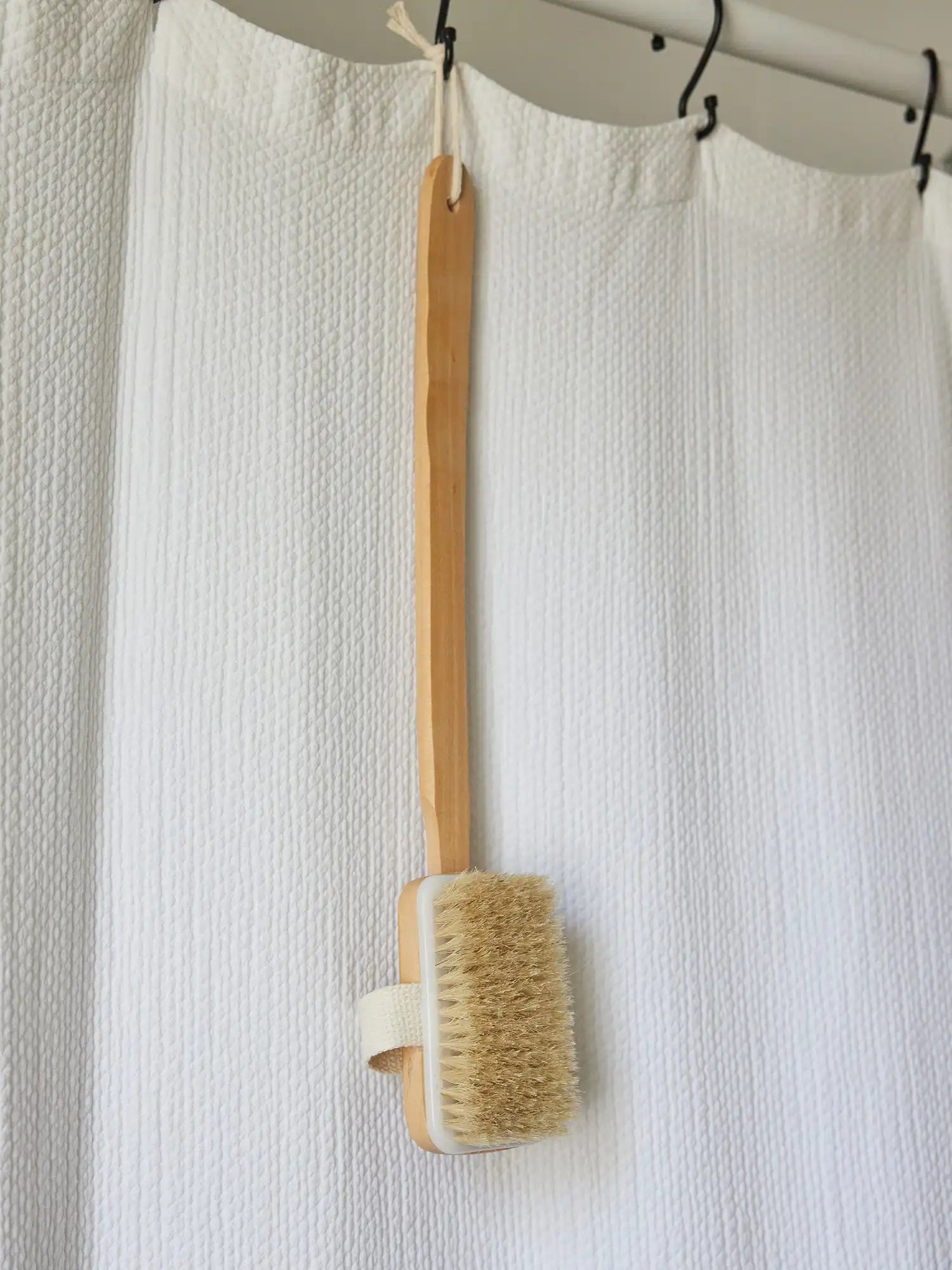 Long-handled bath brush from Juniper Loft Soap Company hanging from a white shower curtain