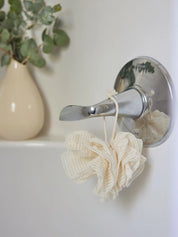 Ramie mesh pouf from Juniper Loft Soap Company hanging from a bathtub lever