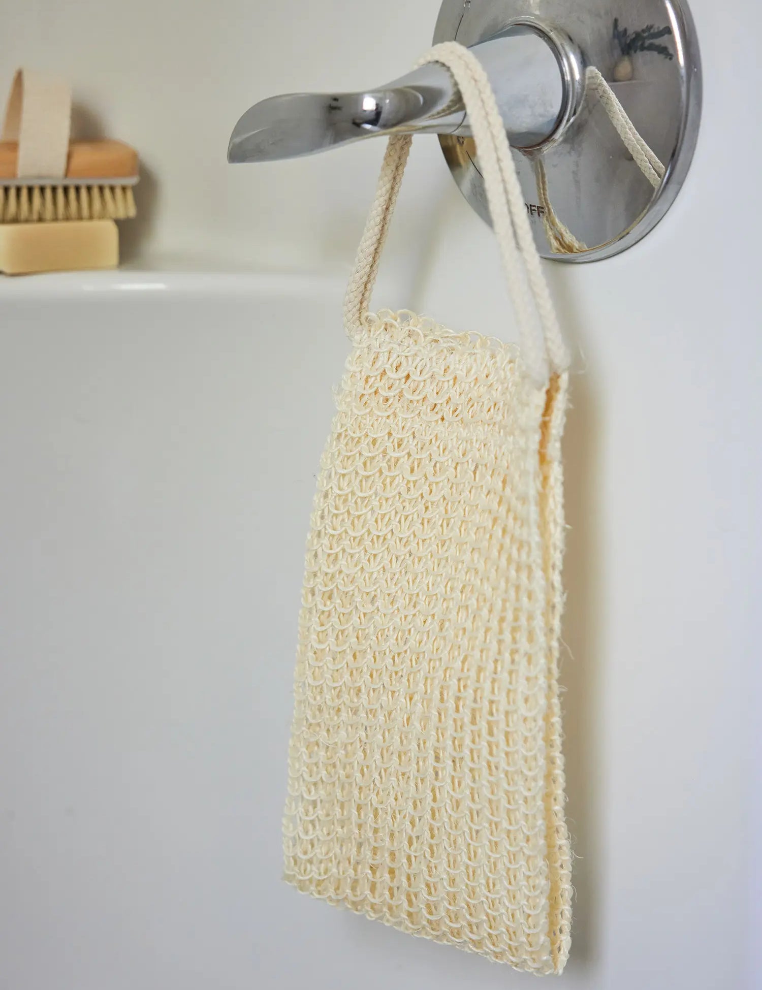 Juniper Loft Soap Company sisal back scrubber hanging from a bathtub lever