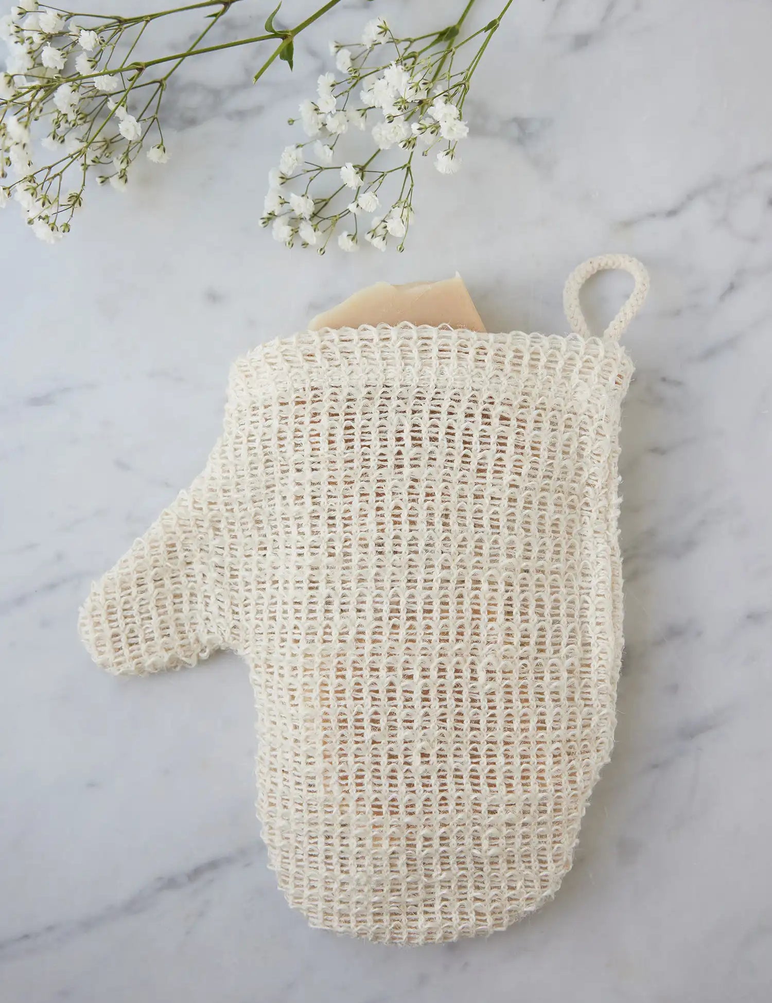 Top view of a sisal mitt from Juniper Loft Soap Company with a bar of soap inside on a gray marble countertop