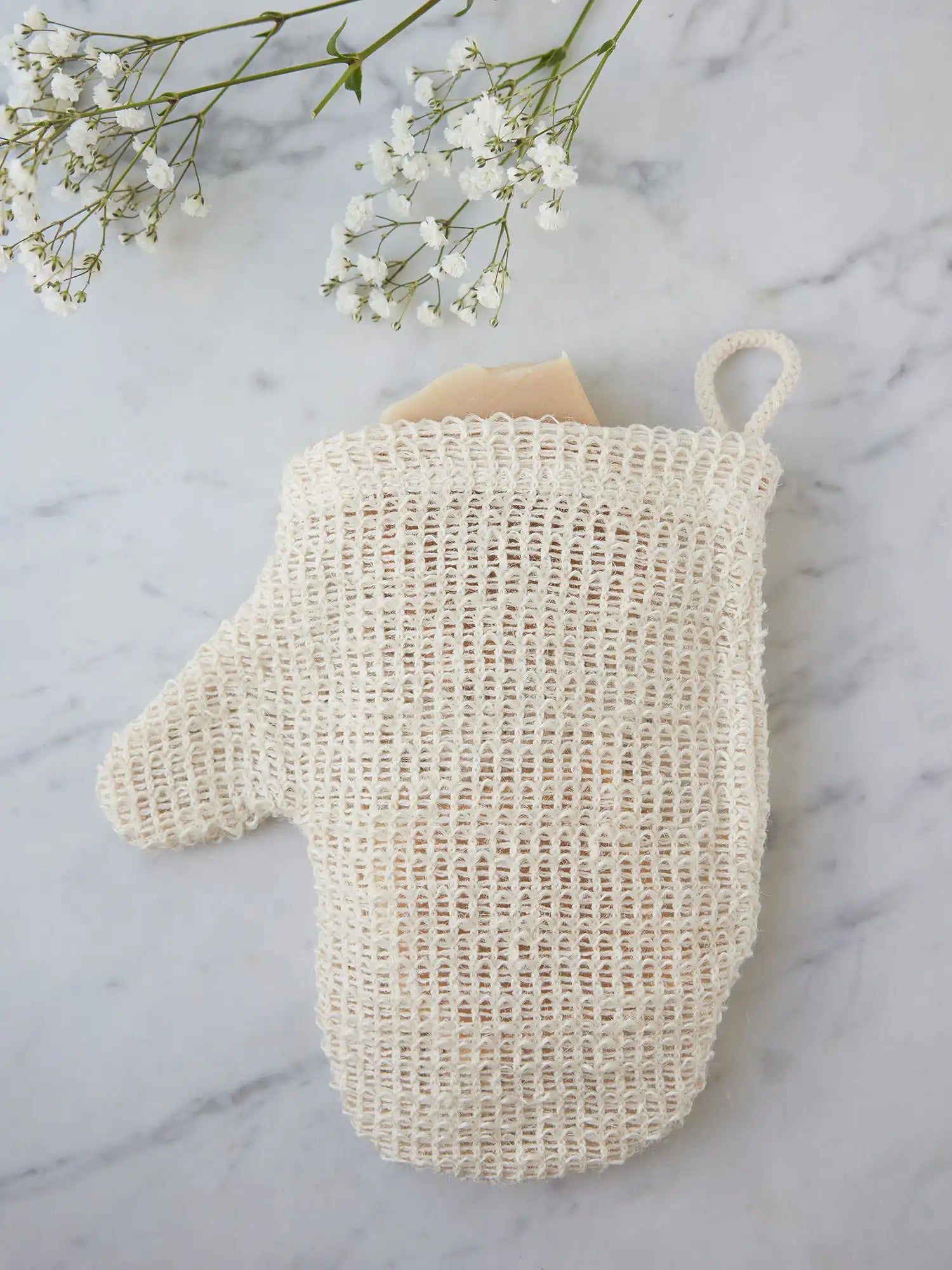 Top view of a sisal mitt from Juniper Loft Soap Company with a bar of soap inside on a gray marble countertop