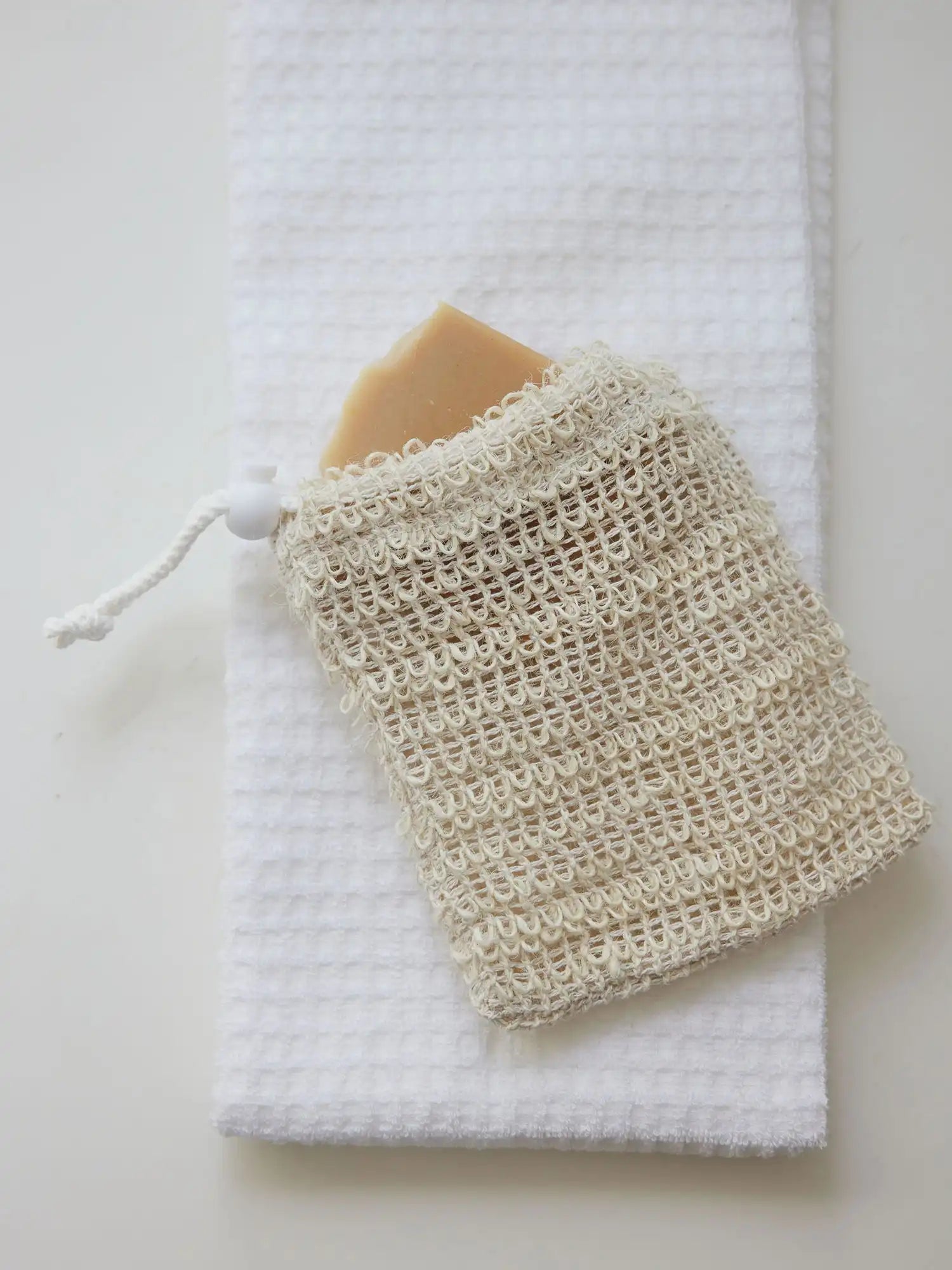 Sisal pouch from Juniper Loft Soap Company with a bar of soap inside on a white towel