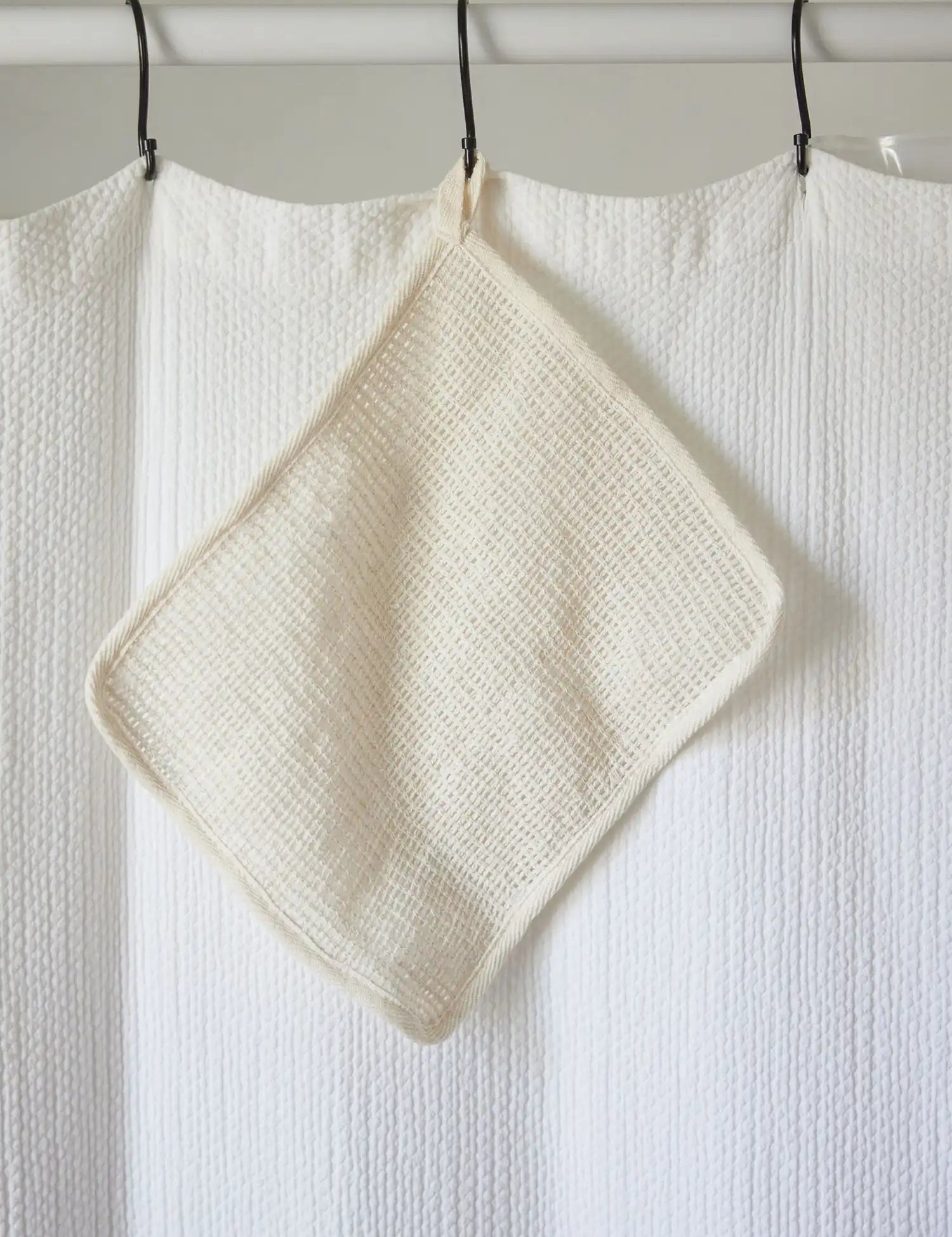 Sisal washcloth from Juniper Loft Soap Company hangs on a white shower curtain