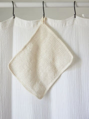 Sisal washcloth from Juniper Loft Soap Company hangs on a white shower curtain