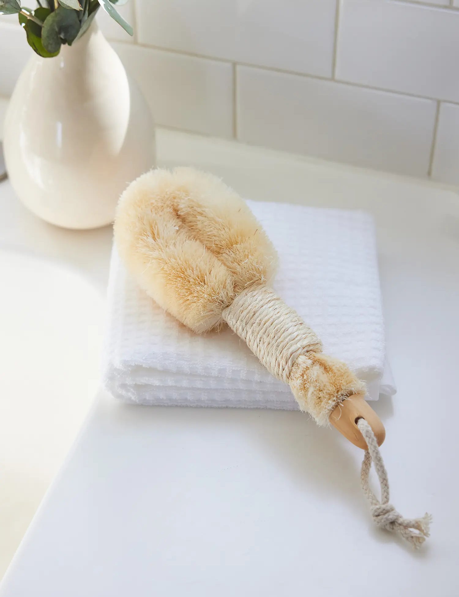 Skin-Smoothing Body Brush from Juniper Loft Soap Company lays on a white towel on a bathroom counter