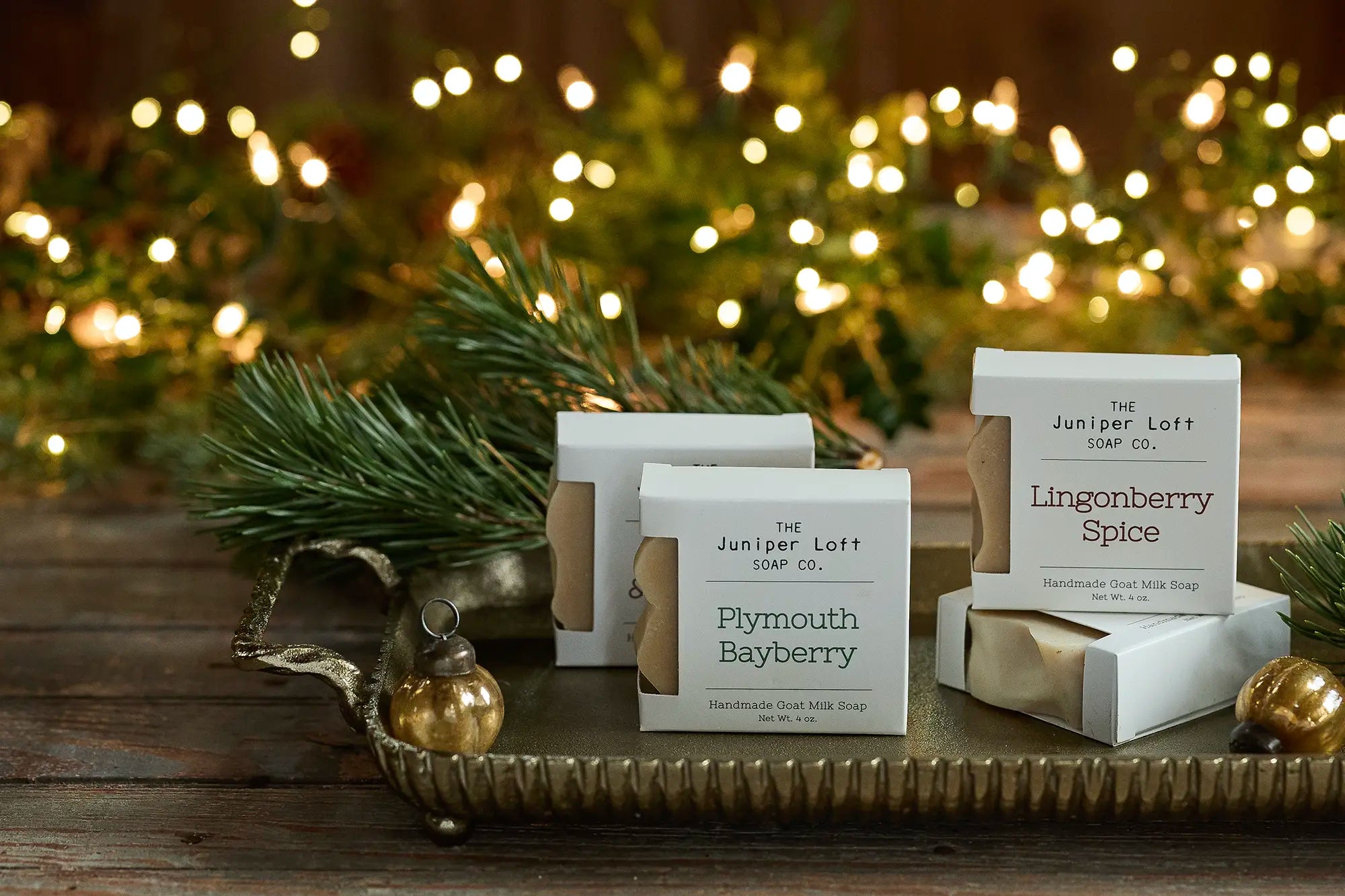 Boxes of Juniper Loft soap in Plymouth Bayberry and Lingonberry Spice scents on a gold tray with sparkly white lights