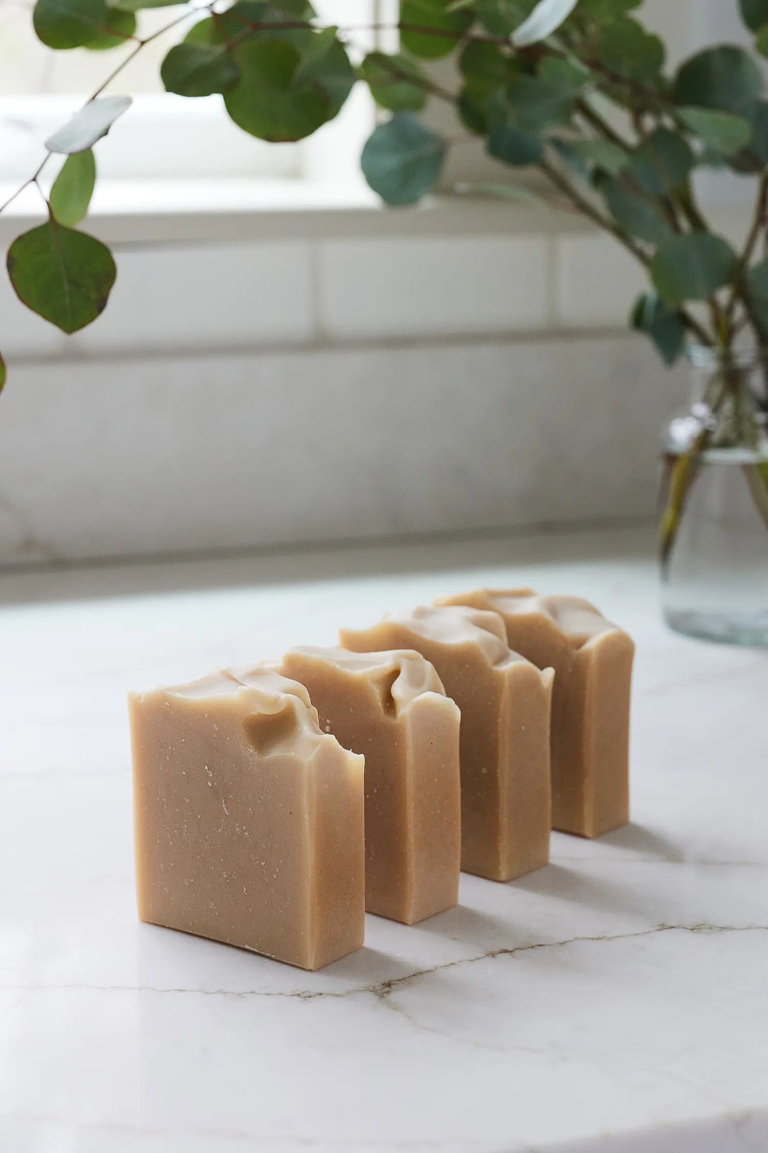 Four bars of soap arranged on a marble surface with a plant in the background.